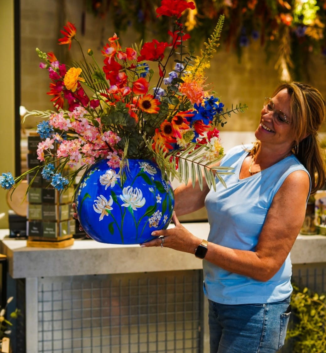 Nicolette met een handbeschilderde blauwe vaas en bloemboeket in de winkel